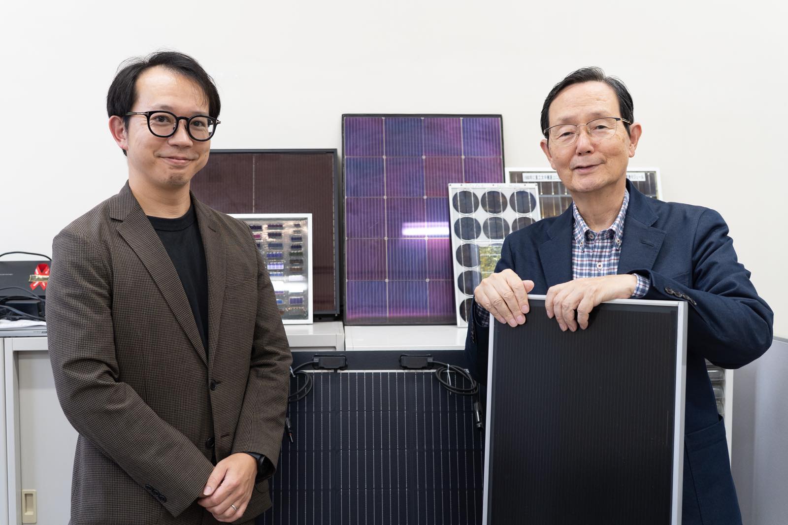 並んで写る小長井特別教授(右)と石川教授(左)。研究室には様々な形状やサイズの太陽電池パネルが並ぶ。
